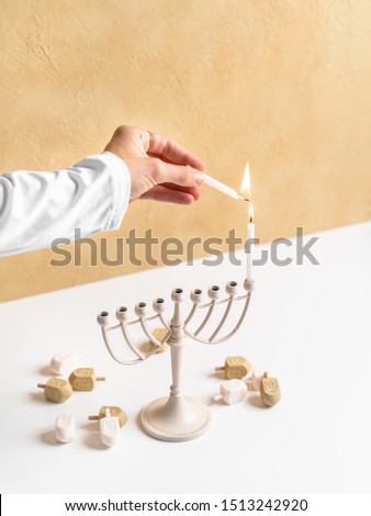 Lighting candles on a menorah for the Jewish holiday of Chanukah. Celebrating the Hebrew holiday Hanukkah with dreidels as a hip young adult in a neutral color palette. 