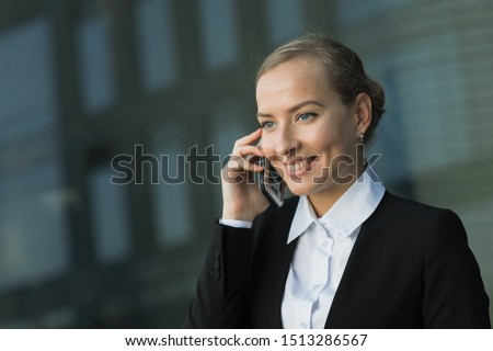 Business portrait of a happy and stylish beautiful young woman in glasses talking with a smile on a smartphone with her friend against the background of office windows. Girl in summer city. Summertime