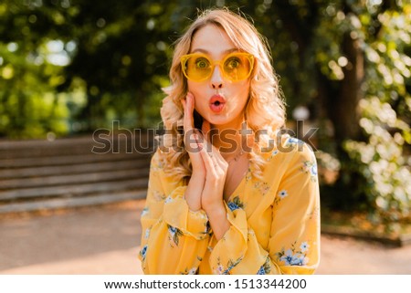 attractive blond stylish surprised woman in yellow blouse wearing sunglasses, colorful summer fashion trend, bright sunny day, positive happy mood