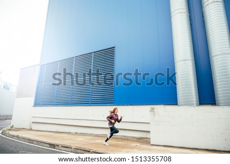 Slim woman running together a blue wall in sportswear