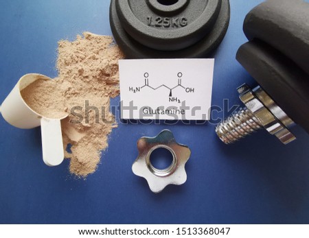Whey protein powder scoop, food supplement for training and exercise with structural chemical formula of glutamine amino acid and dumbbells in the background. Bodybuilding supplement, sport nutrition. Royalty-Free Stock Photo #1513368047