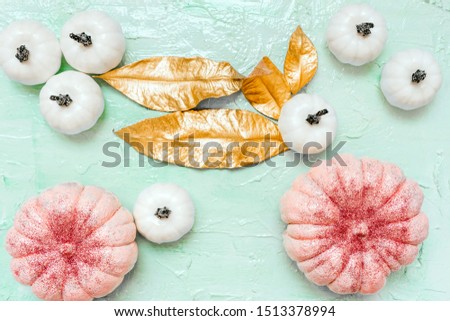 Pink and white pumpkins with glitter and gold leaves on neo mint background, creative concept. Festive advertising flat lay banner. Halloween decor celebration. Trendy composition color, copy space