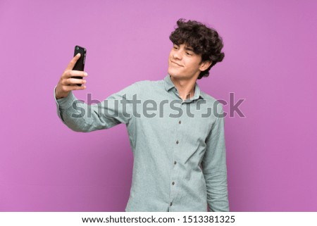 Young man over isolated purple wall making a selfie