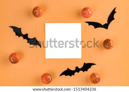 Halloween composition. Pumpkins, bats and paper blank on pastel orange background. Flat lay, top view, copy space