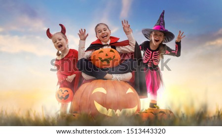 Happy girls on Halloween. Funny kids in carnival costumes outdoors. Cheerful children and pumpkins on sunset background.                               