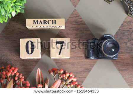 March 7, Date design with Number cube, a flower and camera on Diamond wood background.