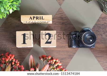 April 12, Date design with Number cube, a flower and camera on Diamond wood background.