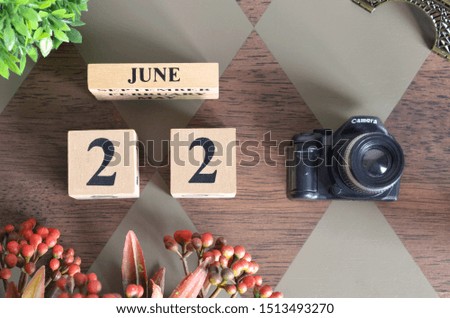 June 22, Date design with Number cube, a flower and camera on Diamond wood background.