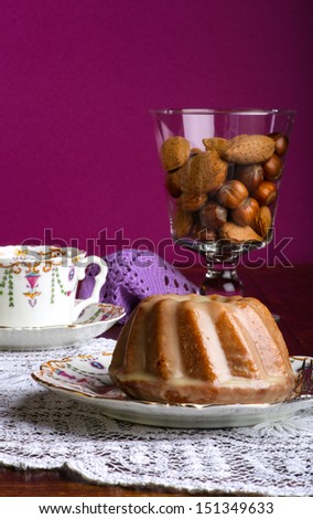 Mini Pound Cake - Almond lemon drizzle on old pictures coffee cup, side plate on lace and glass full of almonds and hazelnuts, purple background