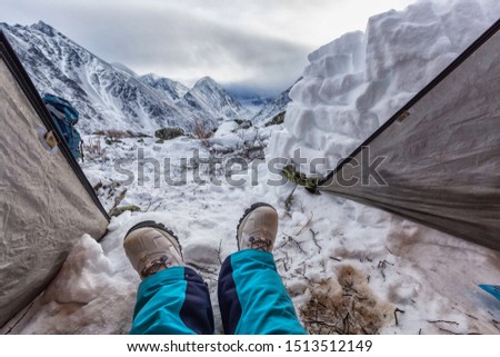 winter in the mountains at the foot of Belukha Mountain. There is a tent and the legs of the person taking pictures are visible from it.