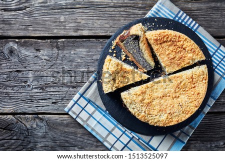 overhead view of delicious Poppy Seed Crumble Cheesecake sliced on a black slate round plate on a rustic wooden table, horizontal view from above, close-up