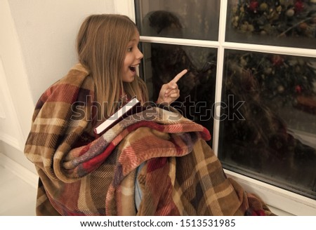 Just look at that. Happy small girl point finger at window. Small reader enjoy reading Christmas story wrapped in plaid. Small child read book on Christmas eve. Childrens book. Magic xmas spirit.