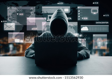 Hacker at dark desktop using laptop with digital business interface hologram on blurry night city background. Big data and virus concept. Double exposure 