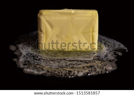A cube of butter melting on a black plate on black isolated background. Royalty-Free Stock Photo #1513581857