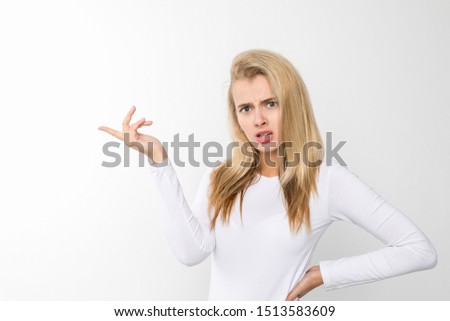 Self assured female holding hand on waist and pointing aside while standing against white background and looking at camera
