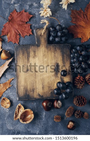 Autumn composition with cutting wooden board, marple leaves, freshly harvested ripe grapes, cones and wallnuts on dark stone table. Cozy autumn concept