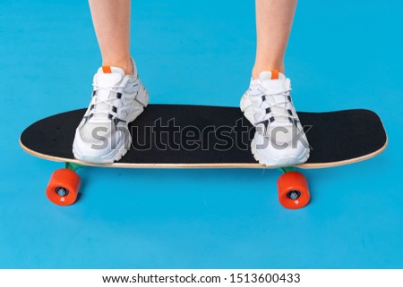 Teenager girl standing and posing on skateboard over a color background 