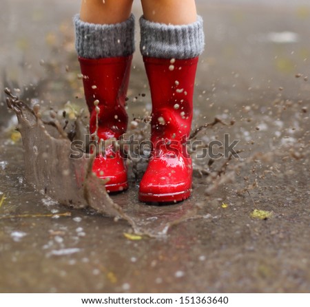 Child wearing red rain boots jumping into a puddle. Close up Royalty-Free Stock Photo #151363640