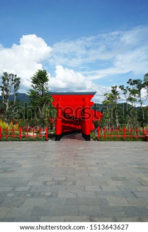 Traditional Japanese Shinto Torii gate among green natural mountain park and cloudy blue sky, the iconically gateways that typically mark the entrance to Shinto shrines traditionally made of wood