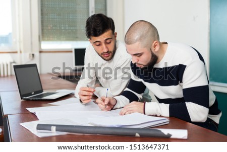 Portrait of two young guys working on their student project at desk in classroom