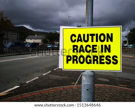 Caution Race in Progress - Sign.  The triathlon bike course travels through the village of Llanberis in North Wales alongside the regular traffic. 