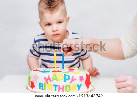 A small child watches as his mother lights candles on the cake