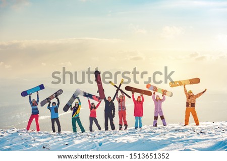 Big group of happy friends skiers and snowboarders having fun and holding ski and snowboards on mountain top