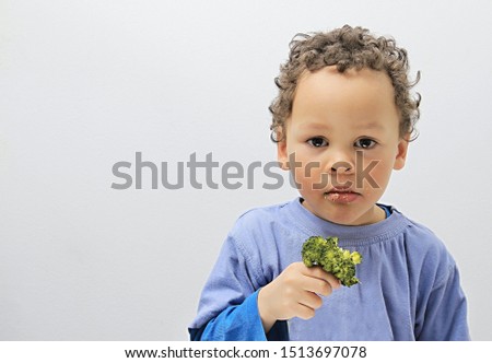 little boy eating broccoli with grey background stock photo