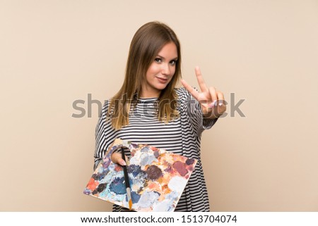 Teenager girl holding a palette over isolated background smiling and showing victory sign