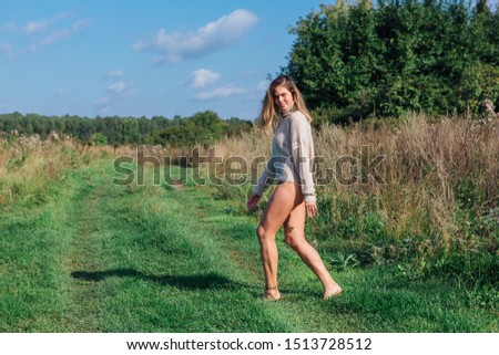 Happy young beautiful woman dressed in a sweater and underpants walking in a green field. Young woman smiling, dancing and jumping on a green grass with barefoot
