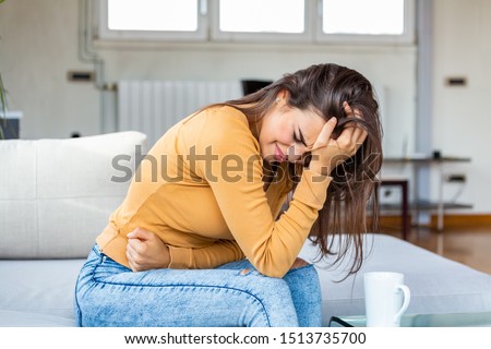 Young sick woman with hands holding pressing her crotch lower abdomen. Medical or gynecological problems, healthcare concept. Young woman suffering from abdominal pain while sitting on sofa at home Royalty-Free Stock Photo #1513735700
