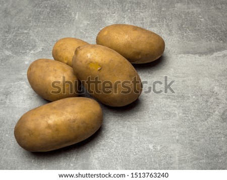 Group of five raw, uncooked, brown potatoes on gray background.