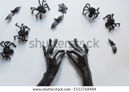 Halloween holiday border of spider, bat and gesture female hands covered black paint with decorations on grey background. Flat lay, top view. Creative Halloween Day composition.