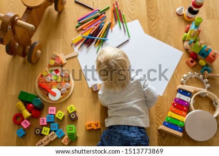Little blonde toddler boy, drawing with pastels and coloring pens, playing with early development wooden toys