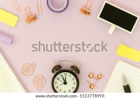 Top view frame with rose gold stationery, pen and notebook, black alarm clock. Mockup female pink desk with copy space