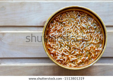 Instant noodles in a deep plate on a wooden table, top view