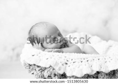 Newborn baby sleeping in basket on white crocheted blanket black and white picture