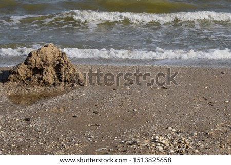 Sand castle on the background of the sea on the beach. Fragile sand house near the sea wave, concept. Landscape view of the horizon line over turquoise sea from sand beach.