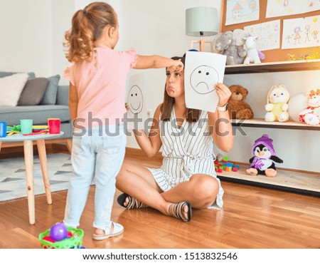 Beautiful psycologist and blond toddler girl sitting on the floor doing therapy using  emotions at consulting room
