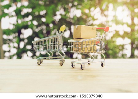 Online shopping and delivery service concept.Brown paper boxs in a shopping cart on wood table on the public park background.Easy shopping with finger tips for consumers.