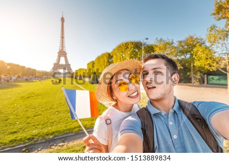 Mixed race couple in love hugging and taking selfie with french flag and Eiffel tower in the background. Honeymoon travel in France and Paris concept