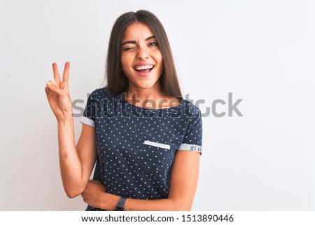 Young beautiful woman wearing blue casual t-shirt standing over isolated white background smiling with happy face winking at the camera doing victory sign. Number two.