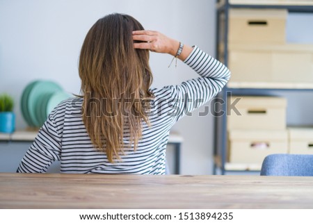 Middle age senior woman sitting at the table at home Backwards thinking about doubt with hand on head