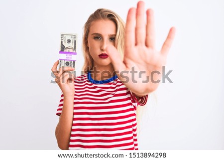 Beautiful woman wearing red striped t-shirt holding dollars over isolated white background with open hand doing stop sign with serious and confident expression, defense gesture