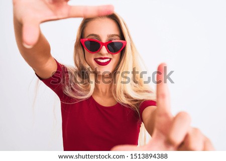 Young beautiful woman wearing red t-shirt and sunglasses over isolated white background smiling making frame with hands and fingers with happy face. Creativity and photography concept.