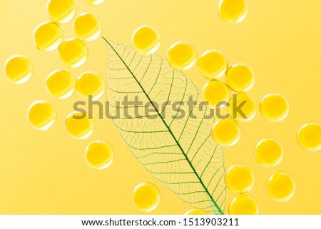 Macro skeletonized green leaves and balls of cosmetic oil on a yellow background photographed in the light. Top view decorative abstraction.