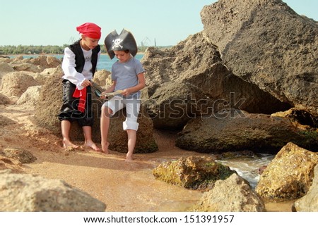 Adorable young boy and girl pirates currently hold the map to find the treasure on a background of a sea landscape