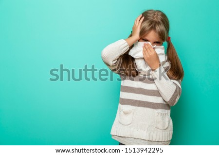 Portrait of a little girl having a flu, fever and headache, blowing and wiping nose with paper tissues