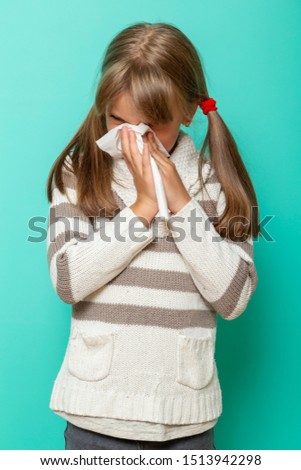 Portrait of a little girl having a flu, blowing and wiping nose with paper tissues on mint colored background