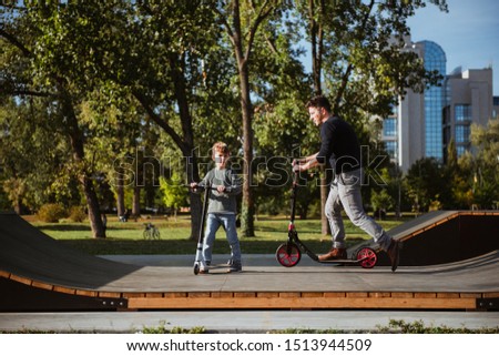 Little boy riding a push scooter with his dad